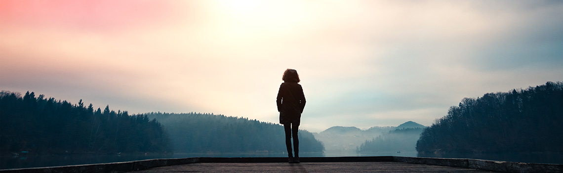 Woman standing on jetty and watching sunrise by the lake.