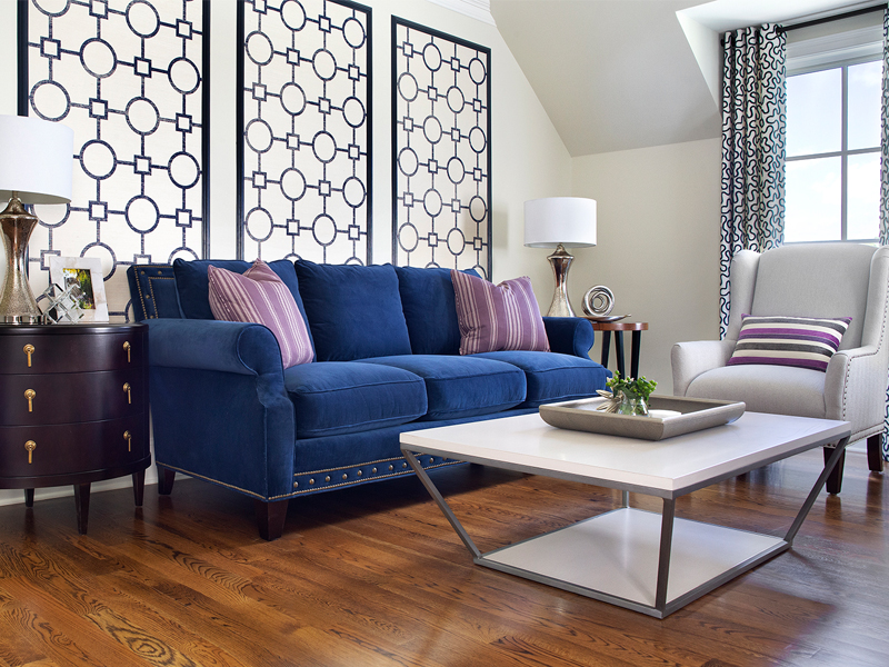 Elegant living room with navy blue sofa, geometric wall panels, and contemporary coffee table on hardwood floors.