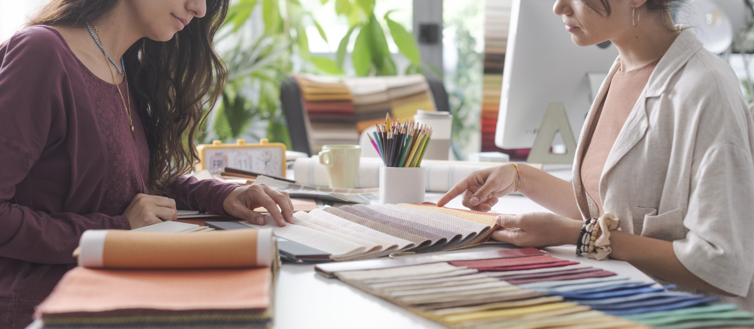 Interior designer and customer sitting at office desk, they are checking fabric swatches and picking colors